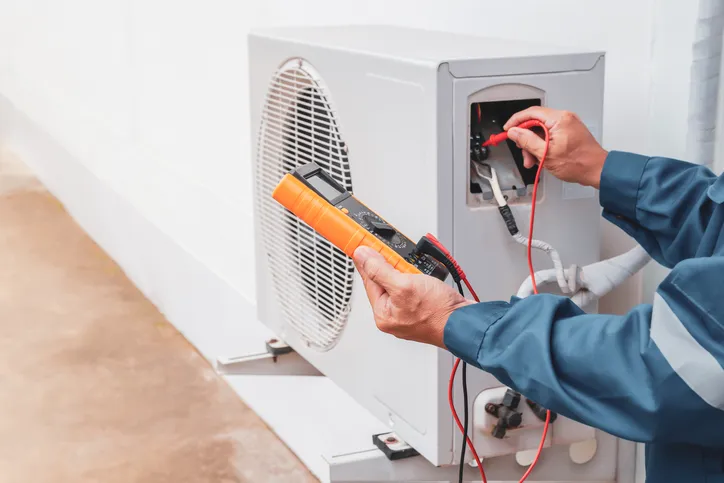 Technician using multimeter on outdoor HVAC unit.