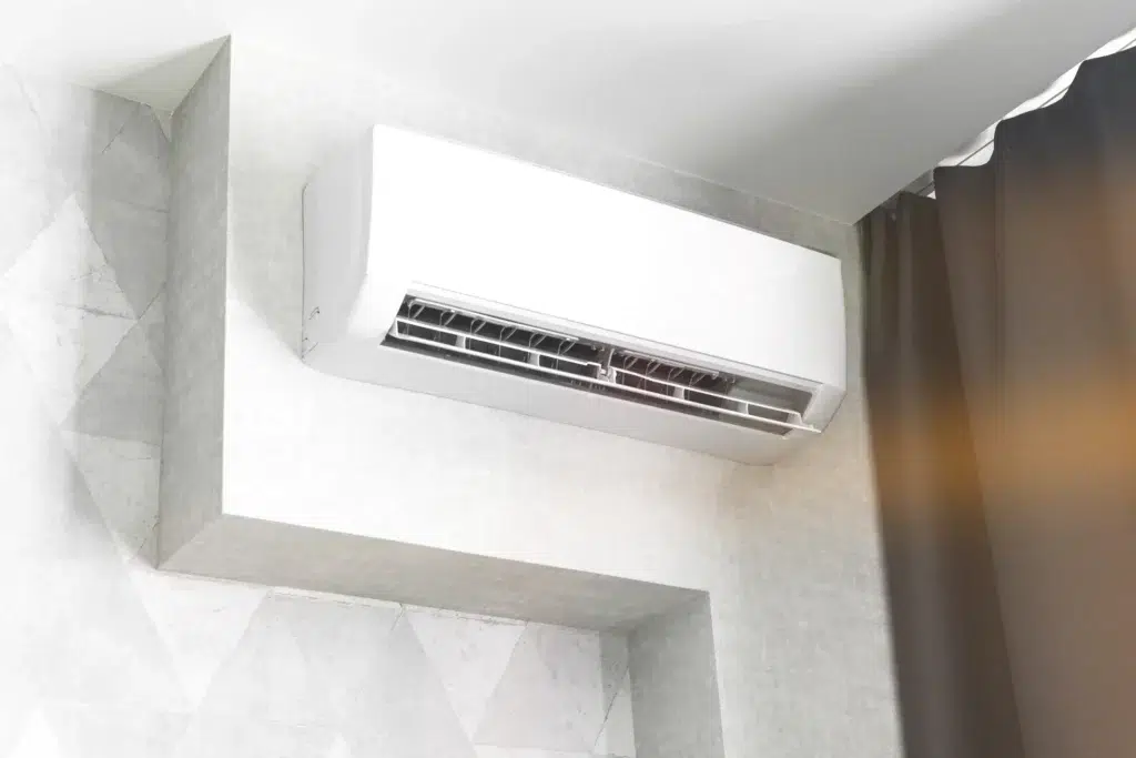 Wall-mounted white air conditioner unit in a modern room with gray textured walls and dark curtains