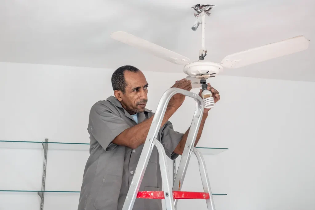 A person is installing a ceiling fan with a light