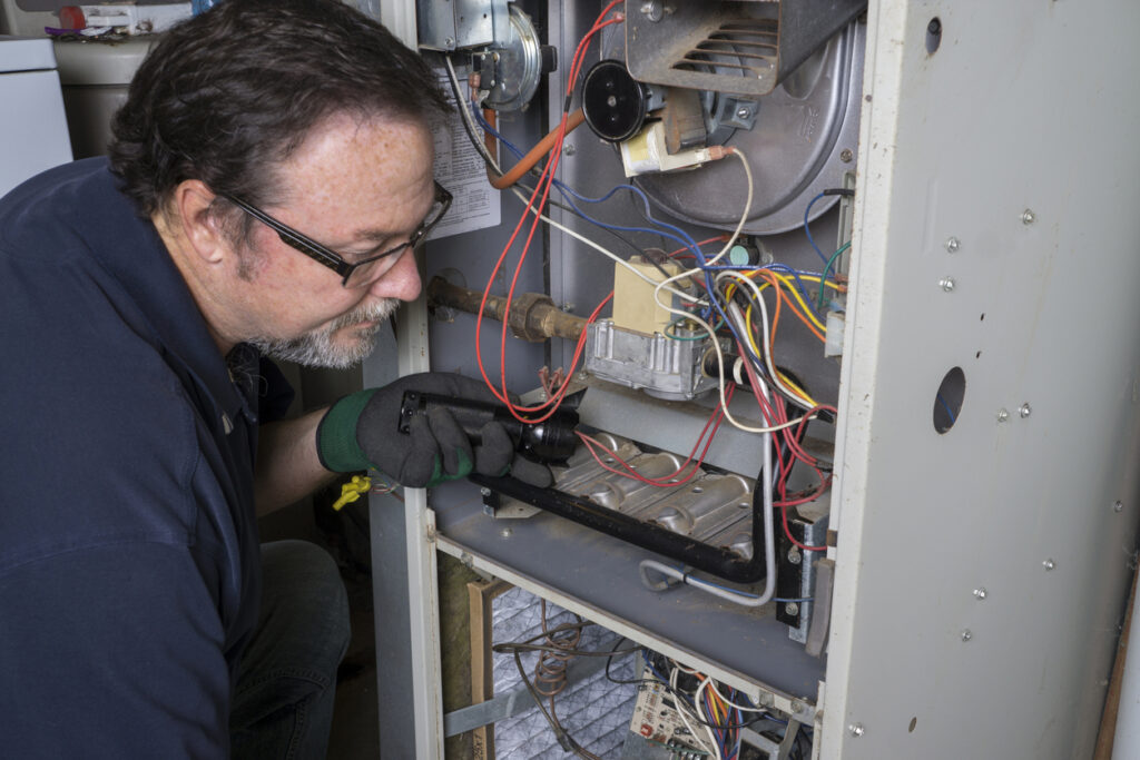 Man in glasses and gloves inspecting the wiring of an open furnace.