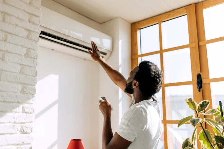 A person adjusting an indoor mini-split air conditioning unit with a remote.
