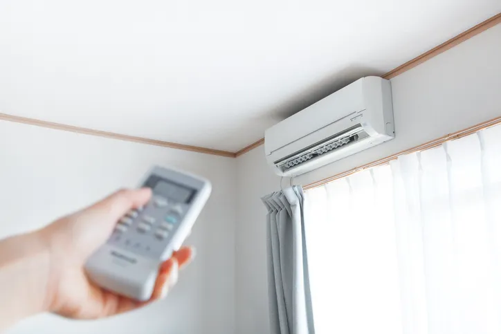 A person's hand holding a remote control pointed at a wall-mounted mini-split air conditioner.