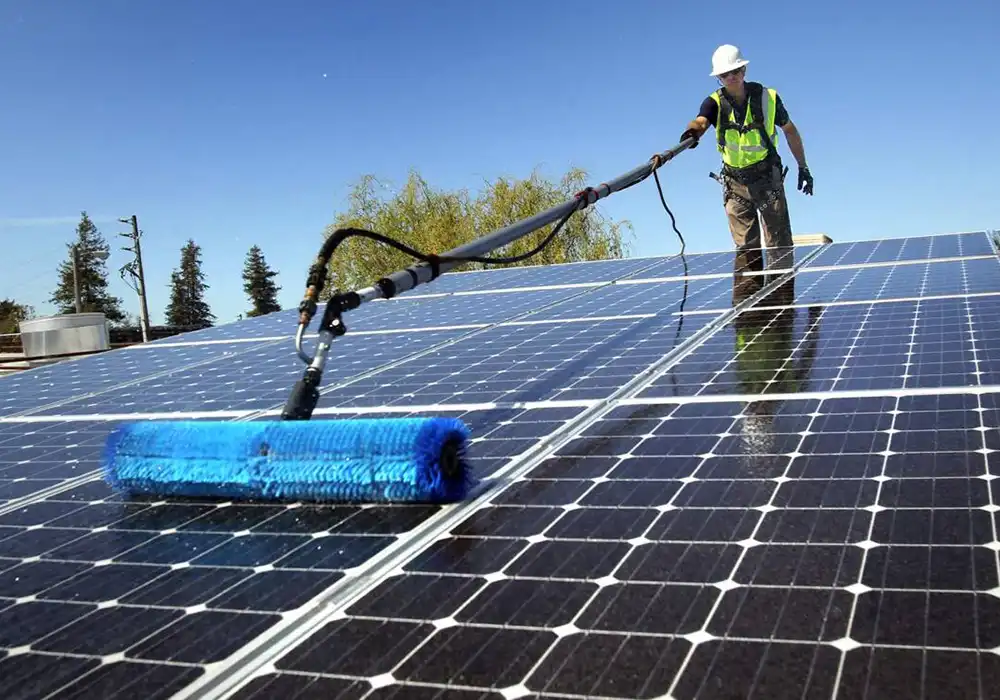 Man cleaning solar panels with long brush.