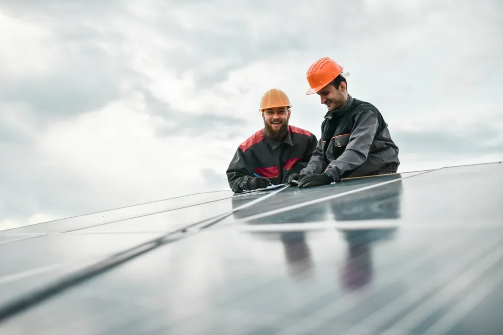 Two technicians wearing orange hard hat standing next to solar panels